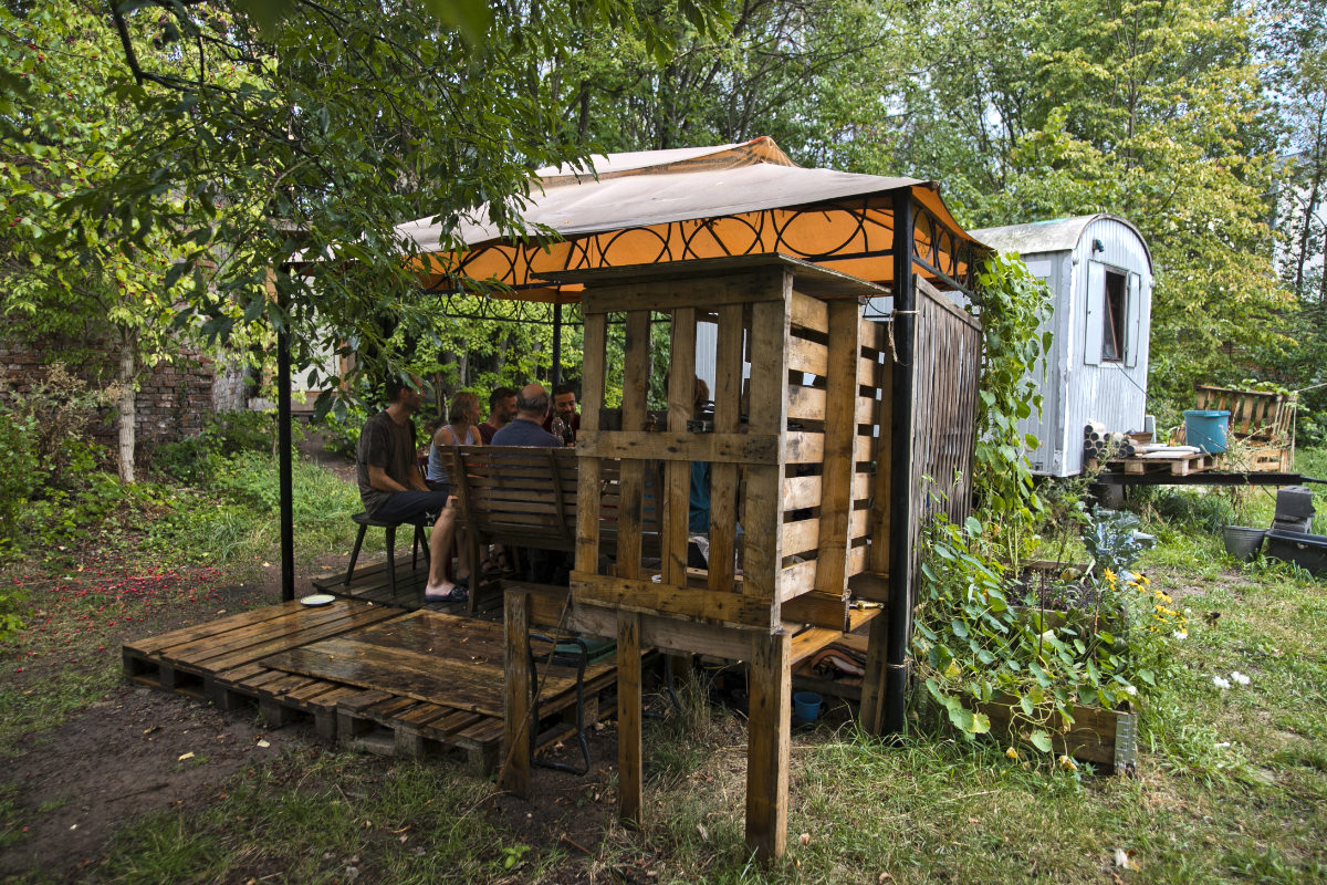Überdachte Sitzplatz in einem Garten mit Bauwagen im Hintergrund